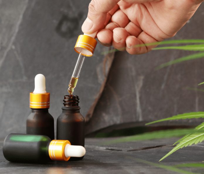 Hand opening CBD oil dropper bottle next to two CBD oil bottles on grey stone marble background