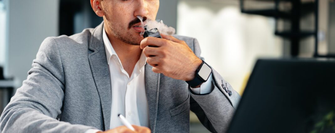 calm man vaping cbd for anxiety in front of laptop