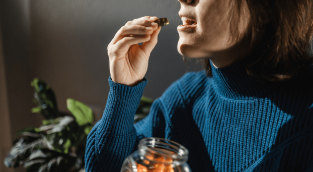 Woman putting CBD gummies into her mouth holding sweets jar