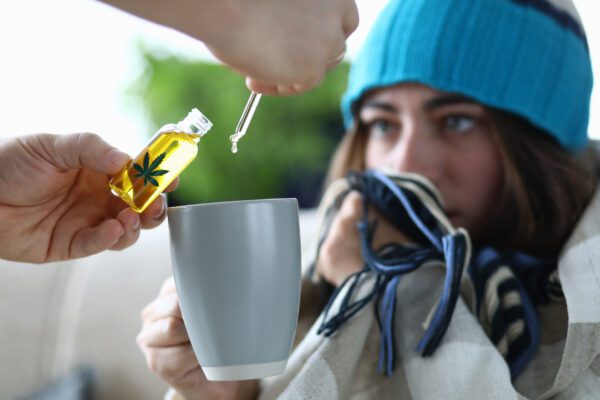 Young woman sick is dripping into cup with drops of CBD extract closeup