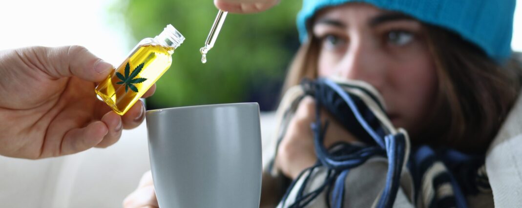 Young woman sick is dripping into cup with drops of CBD extract closeup