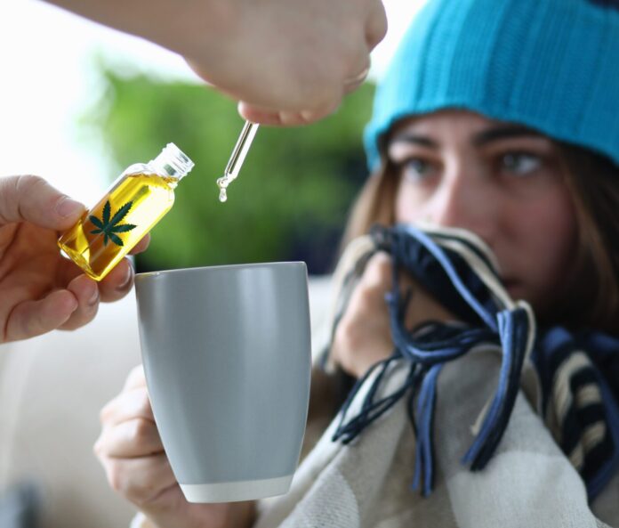 Young woman sick is dripping into cup with drops of CBD extract closeup