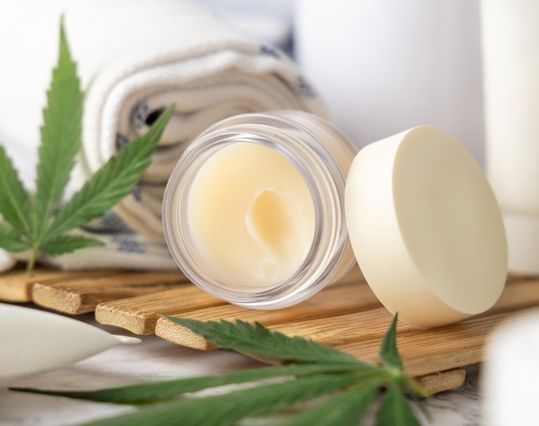 open pot of cbd balm with other skincare product bottles