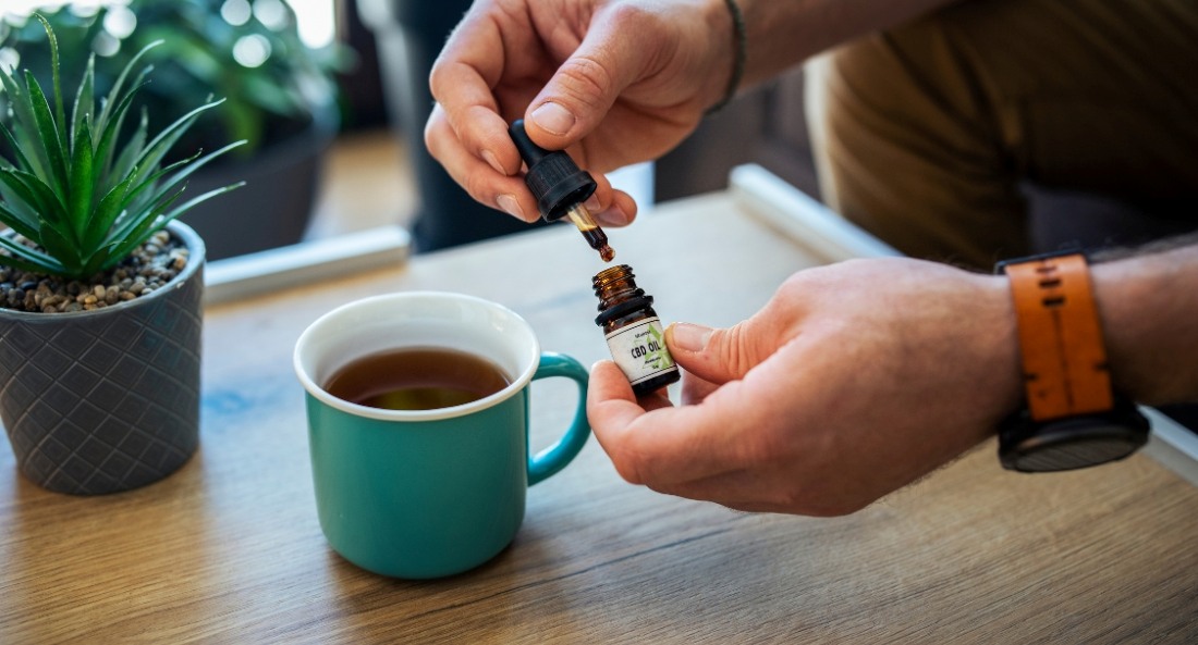 CBD oil bottle being opened over a mug of tea