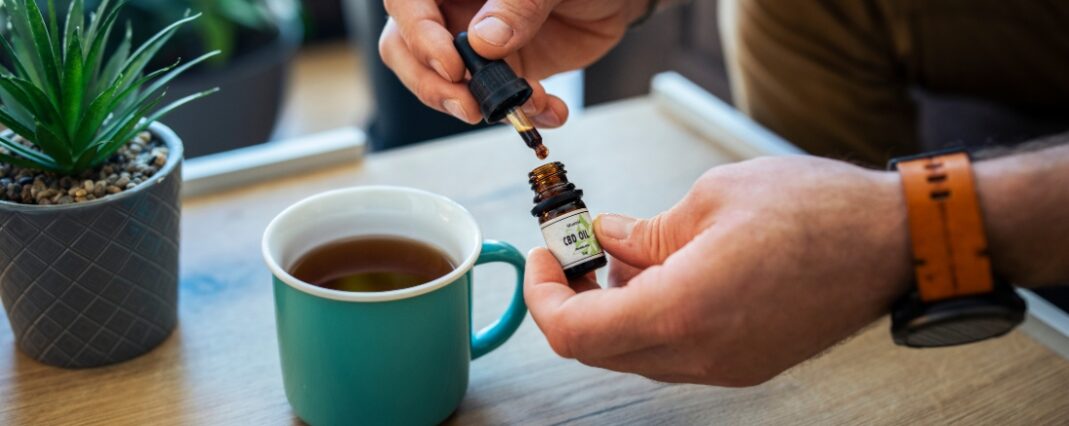 CBD oil bottle being opened over a mug of tea