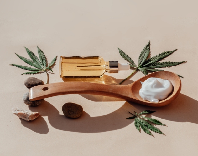 Bottle of cbd oil next to a wooden spoon with cbd moisturiser on it