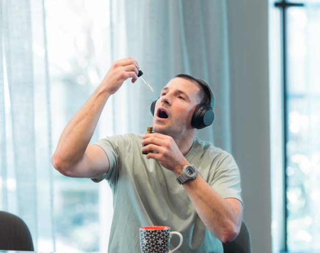 Man with headphones on sitting down taking CBD oil into mouth