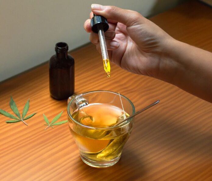 person dropping cbd oil into cbd tea with pipette