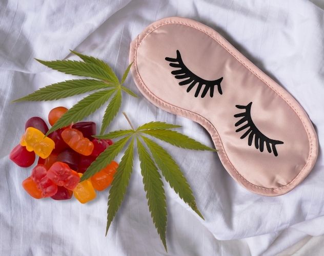 sleep mask and CBD gummies over a bed sheet