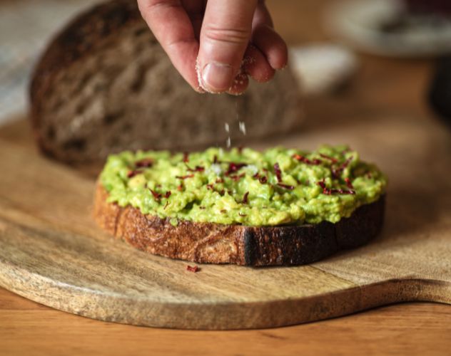 person sprinkling seasoning on avocado toast