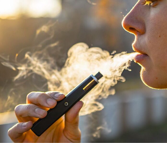 side profile of a boy holding a vape with smoke coming out of his mouth