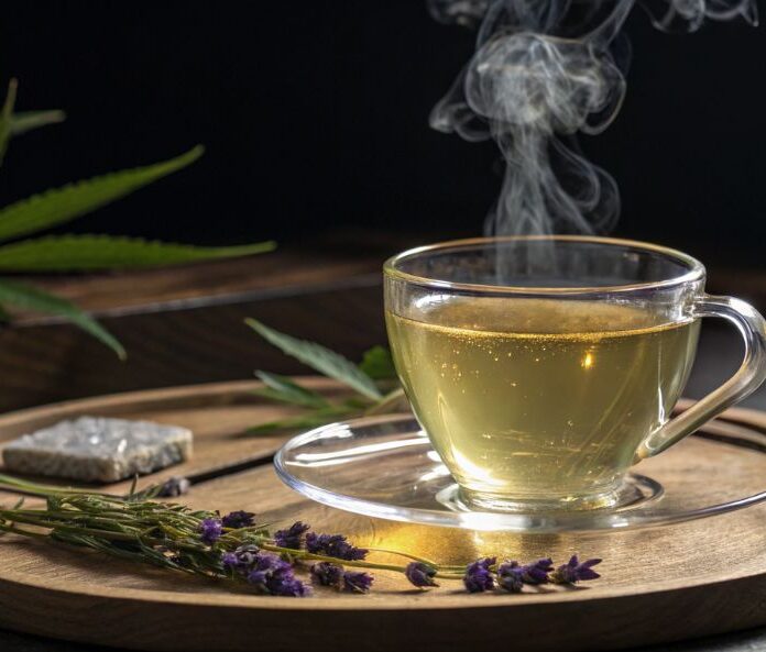 a cup of cbd tea on a round wooden board with pieces of lavender and hemp leaves in the background