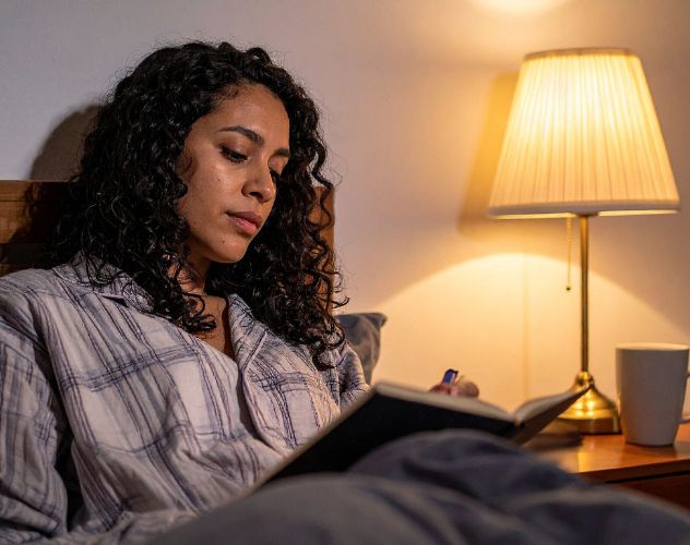 woman reading at night in bed with a bedside lamp on