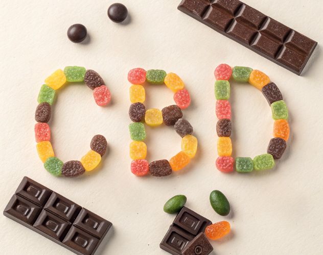 the letters CBD spelled out in fizzy gummy sweets with chocolate bars surrounding it