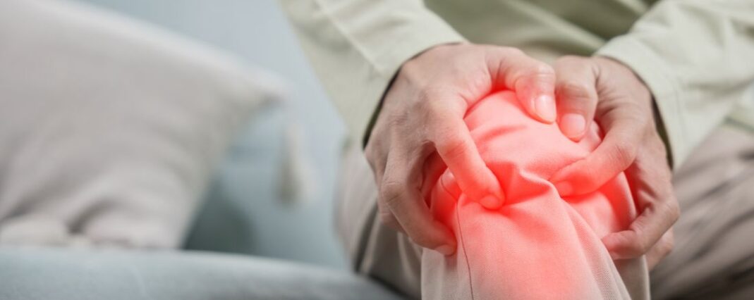 Man sitting on sofa holding knee in pain highlighted in red