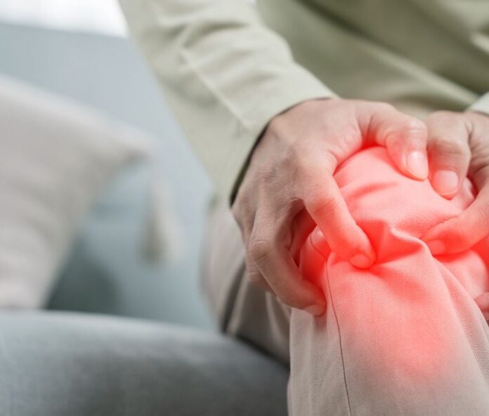 Man sitting on sofa holding knee in pain highlighted in red