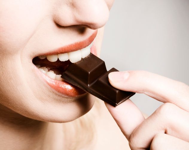 close up of a woman eating a piece of a chocolate bar