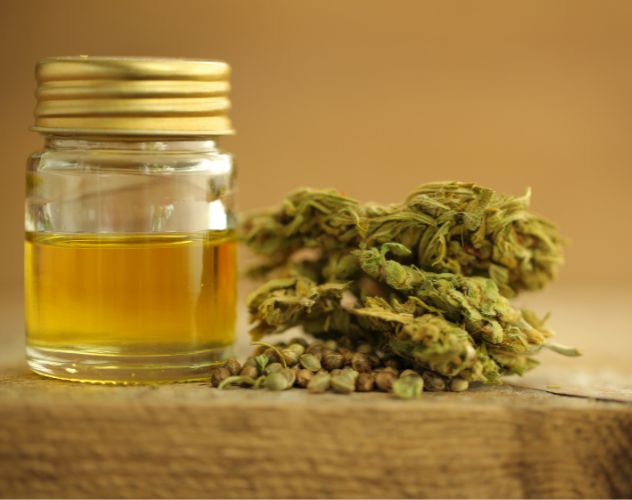 a small pot of cbd oil and cbd flower buds on a wooden board