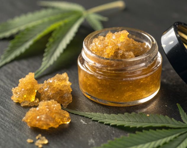 a small glass pot of cbd wax concentrate on a dark surface with hemp leaves