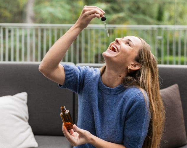 woman dropping cbd oil into her mouth sitting on an outdoor sofa