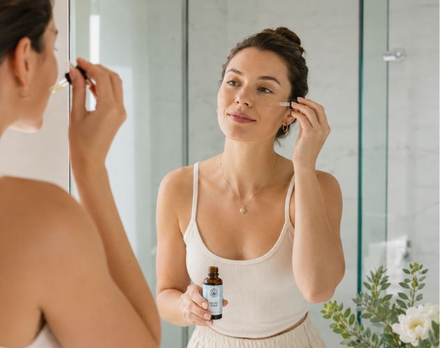 woman applying cbd face serum in the mirror in a bathroom