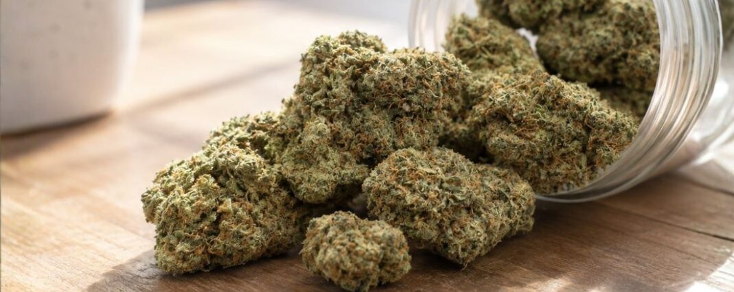 cbd flower buds spilling out a clear jar on a wooden counter