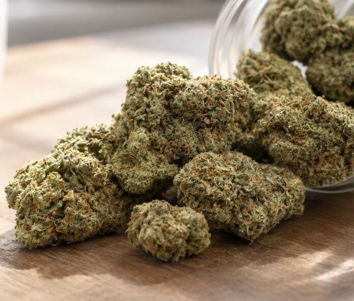 cbd flower buds spilling out a clear jar on a wooden counter
