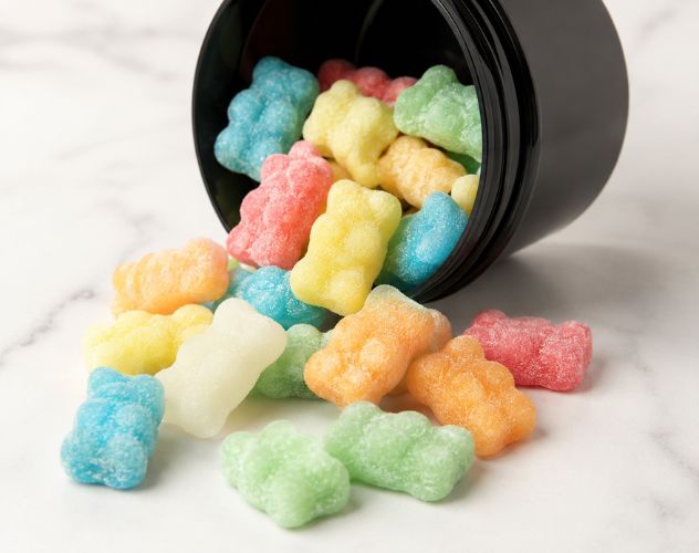 cbd gummy bears spilling out a round black pot on a marble surface